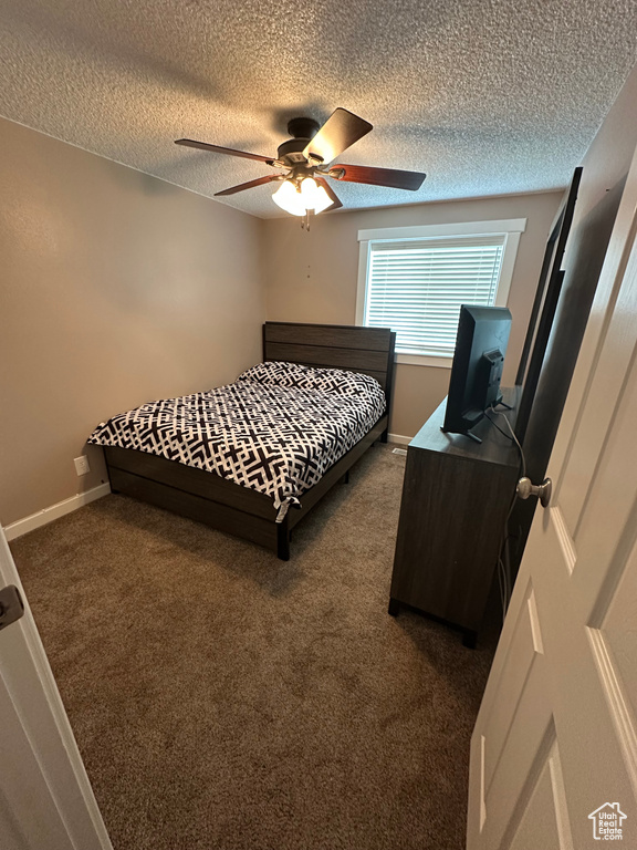 Bedroom featuring a textured ceiling, a ceiling fan, dark colored carpet, and baseboards