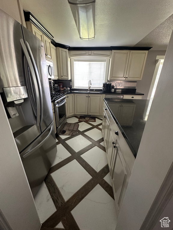 Kitchen with appliances with stainless steel finishes, dark countertops, inlaid floor details, a textured ceiling, and cream cabinets
