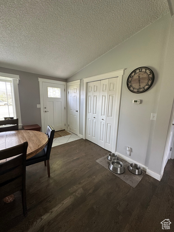 Entrance foyer with a textured ceiling, wood finished floors, vaulted ceiling, and baseboards