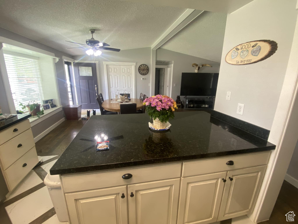 Kitchen featuring ceiling fan, dark stone counters, a textured ceiling, white cabinetry, and vaulted ceiling