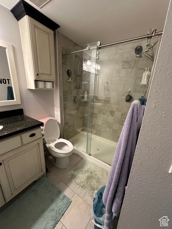 Bathroom with a shower stall, tile patterned flooring, vanity, toilet, and a textured wall