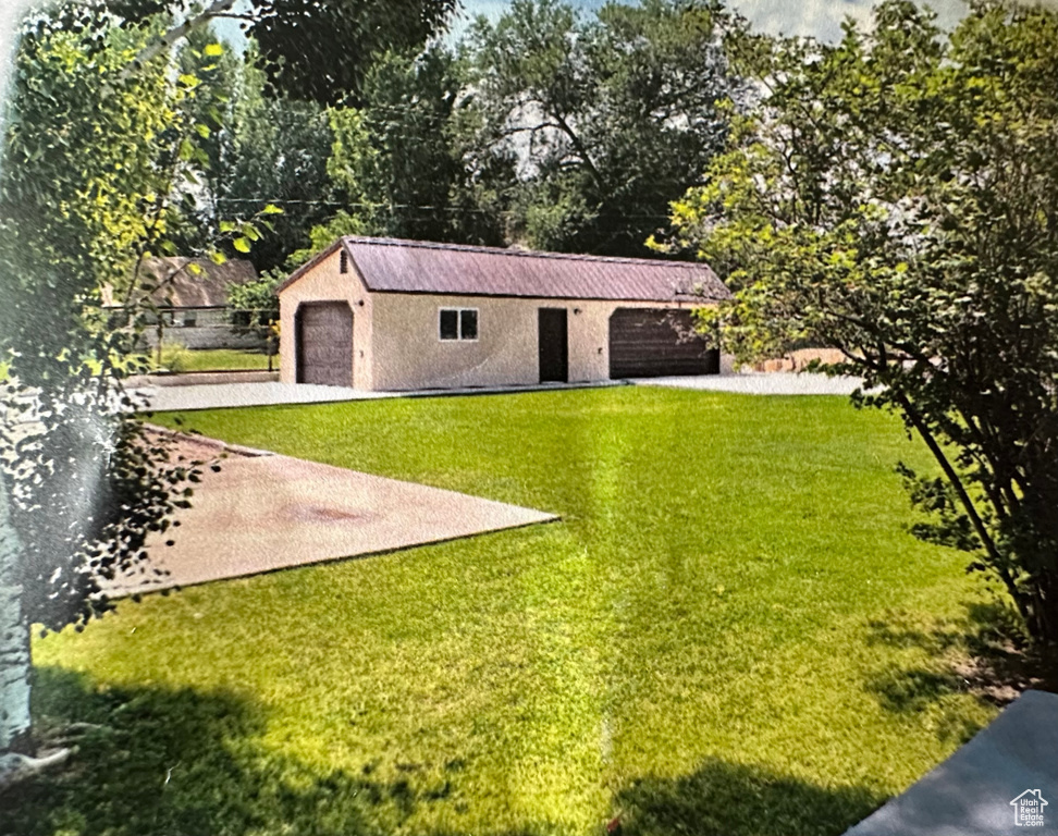 View of green lawn featuring an outdoor structure, concrete driveway, and a detached garage