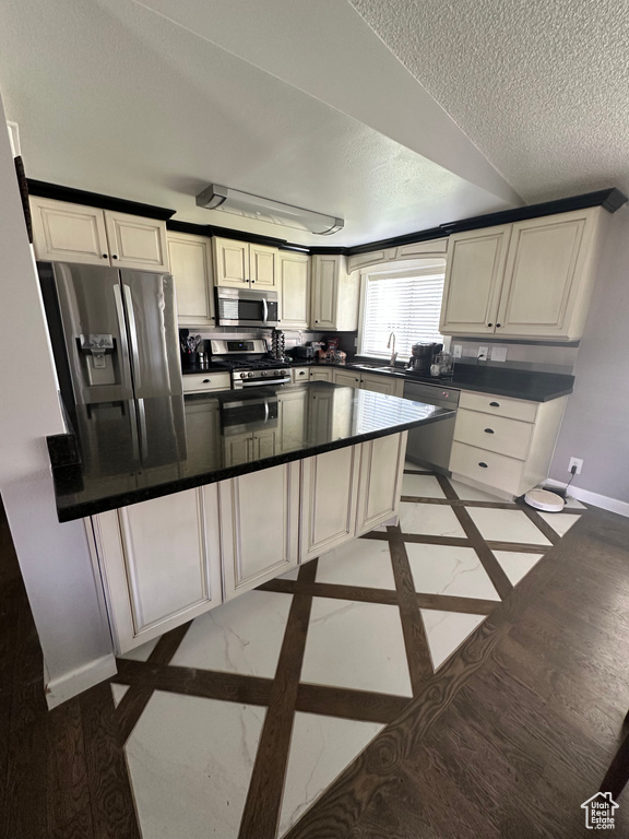 Kitchen with appliances with stainless steel finishes, a textured ceiling, baseboards, dark countertops, and inlaid floor details