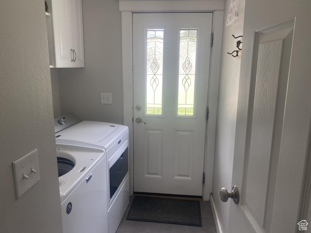 Clothes washing area with washer and clothes dryer, cabinet space, and tile patterned flooring
