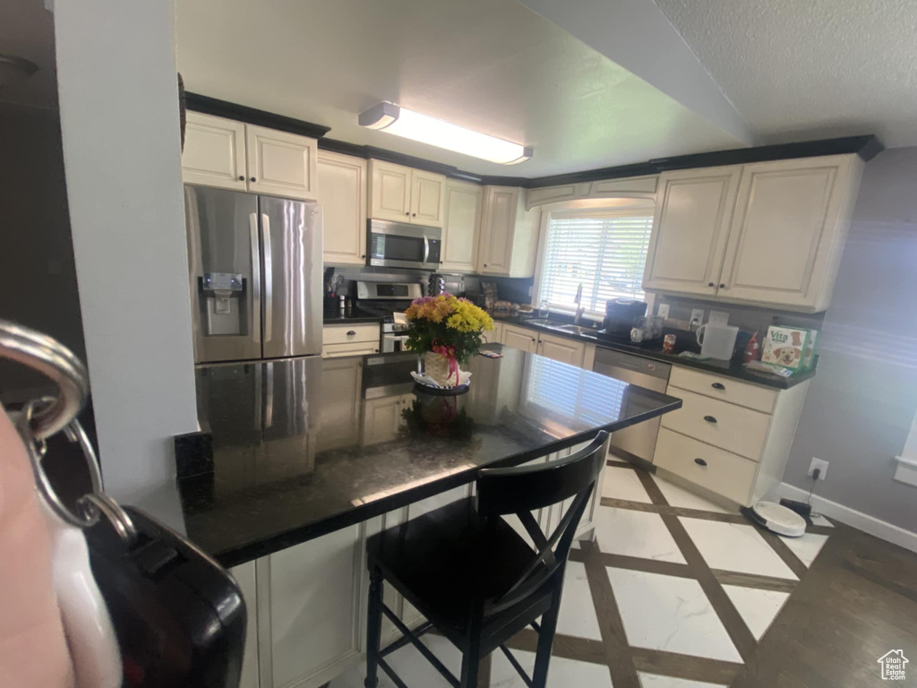 Kitchen featuring stainless steel appliances, dark countertops, baseboards, inlaid floor details, and a textured ceiling