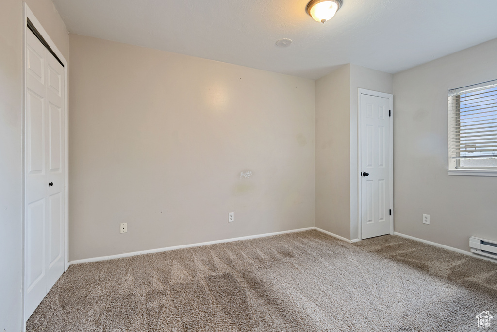 Unfurnished bedroom with carpet flooring, baseboards, and a baseboard heating unit