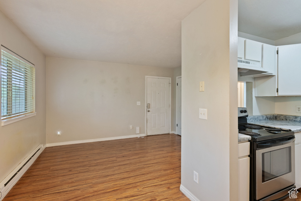 Kitchen with stainless steel electric range, a baseboard heating unit, light wood-type flooring, under cabinet range hood, and light countertops