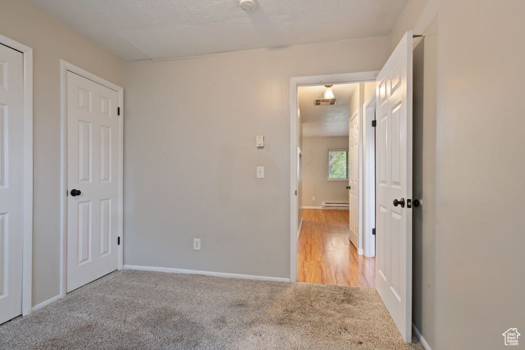 Unfurnished bedroom featuring a baseboard heating unit, light colored carpet, baseboards, and a textured ceiling