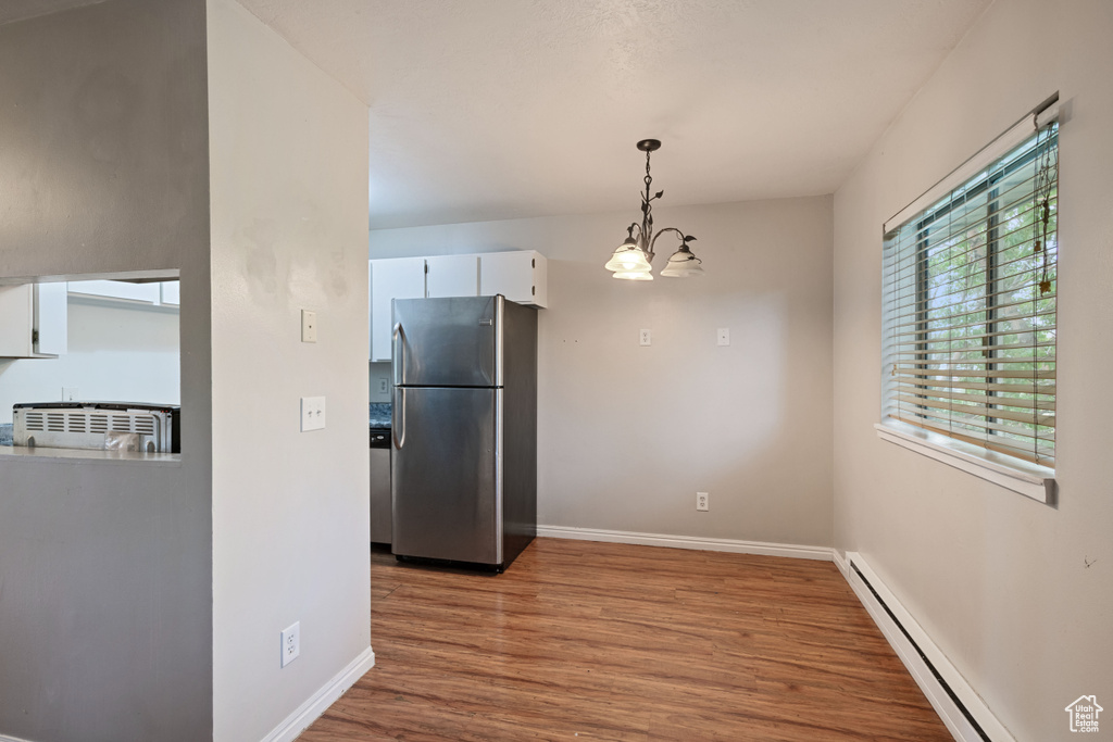 Kitchen featuring freestanding refrigerator, baseboard heating, wood finished floors, white cabinets, and baseboards