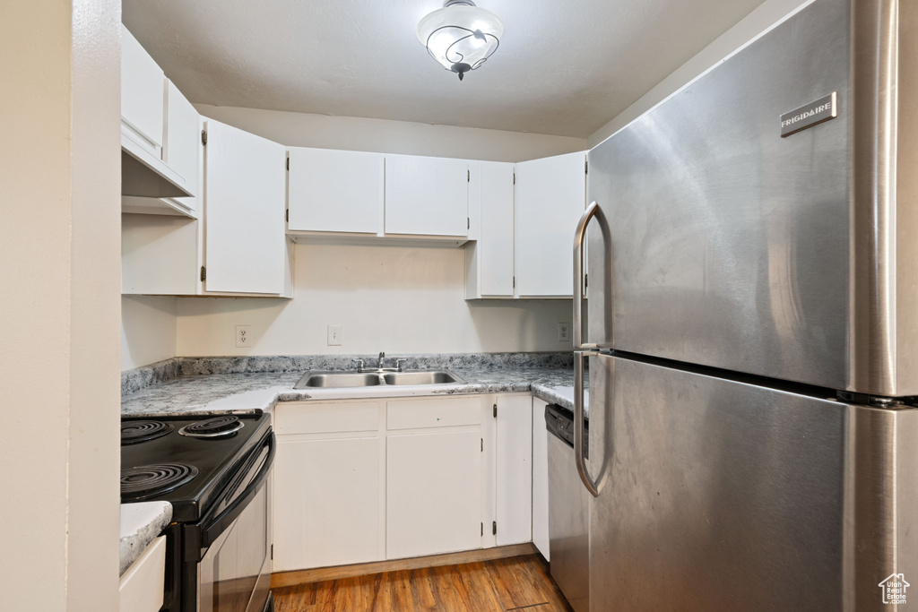 Kitchen featuring stainless steel appliances, a sink, light wood-style flooring, light countertops, and white cabinets