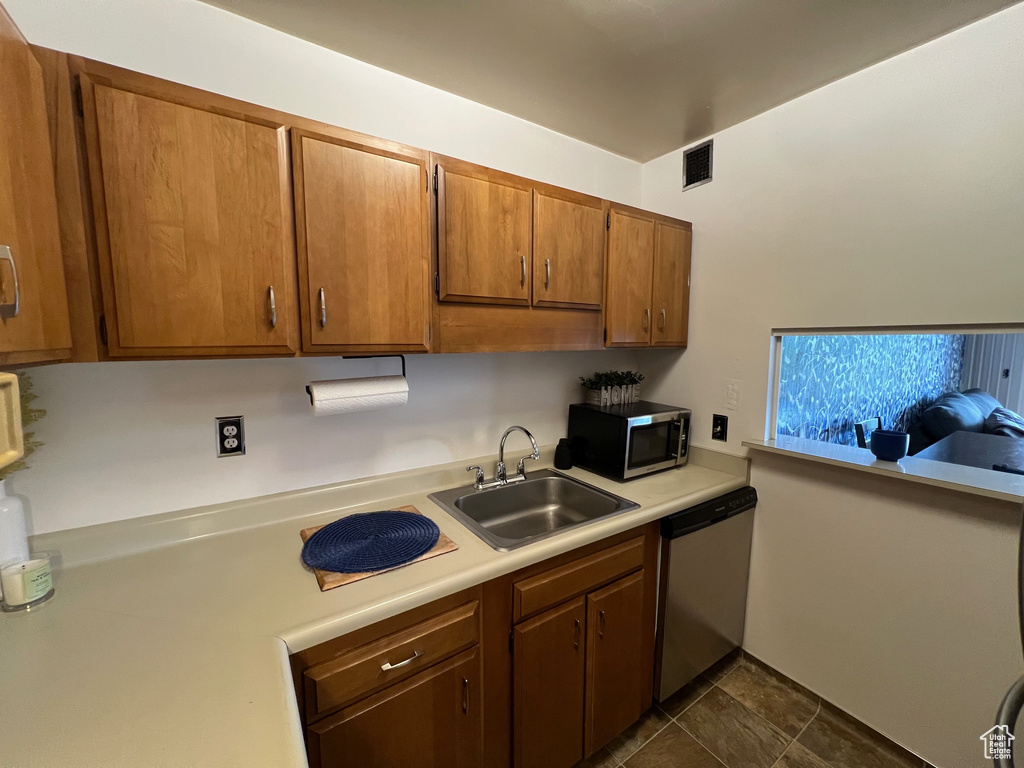 Kitchen featuring stainless steel appliances, light countertops, a sink, and brown cabinetry