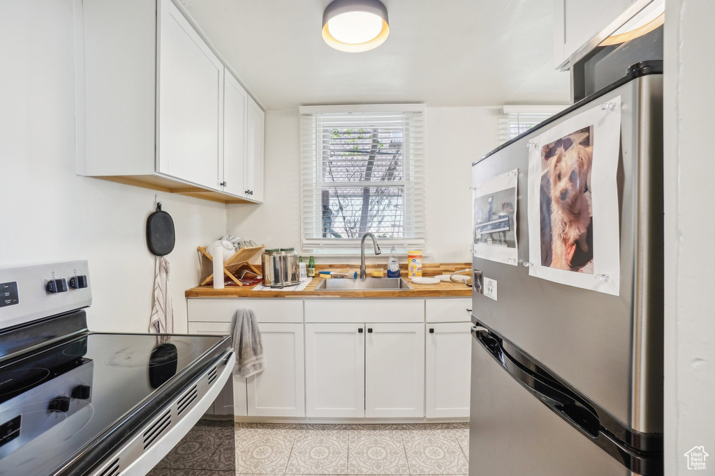 Kitchen with appliances with stainless steel finishes, a sink, white cabinets, light countertops, and light tile patterned floors