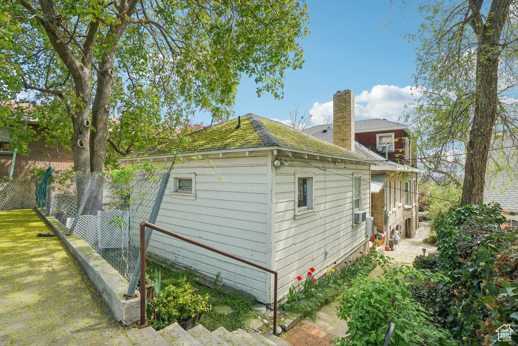 View of side of home with fence, a chimney, a shingled roof, and cooling unit