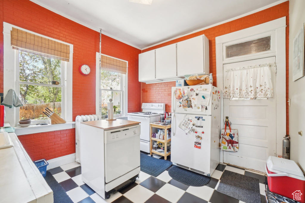 Kitchen with white appliances, tile patterned floors, white cabinets, light countertops, and crown molding