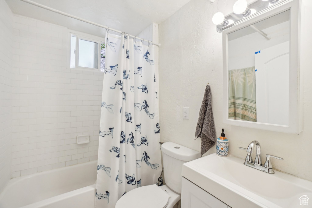 Bathroom with toilet, shower / bath combo with shower curtain, a textured wall, and vanity