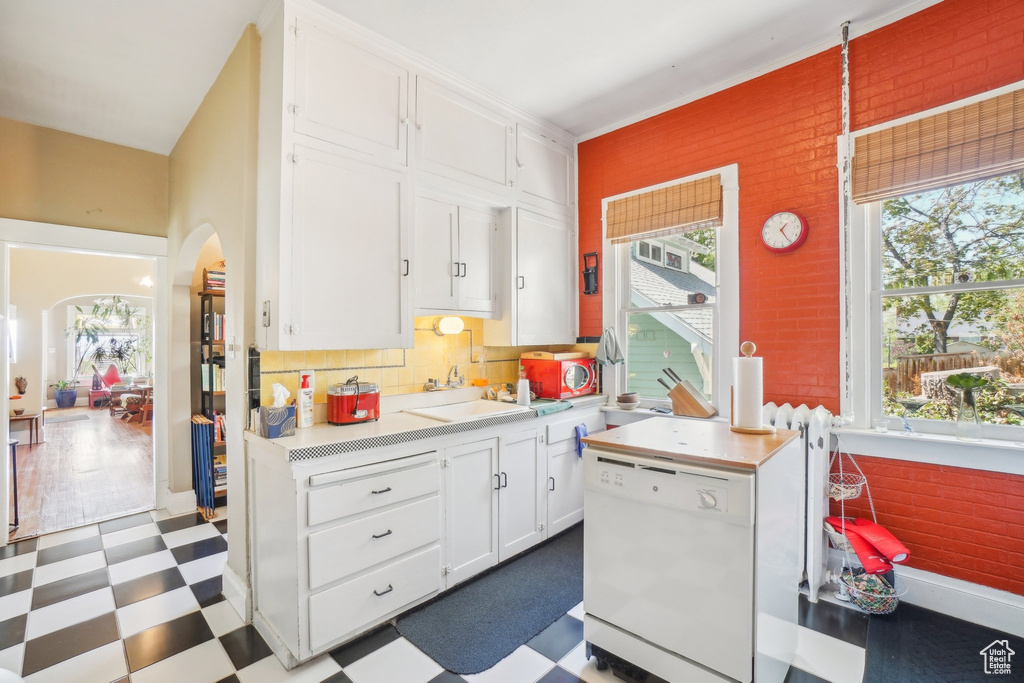 Kitchen featuring dishwasher, dark floors, arched walkways, white cabinets, and light countertops