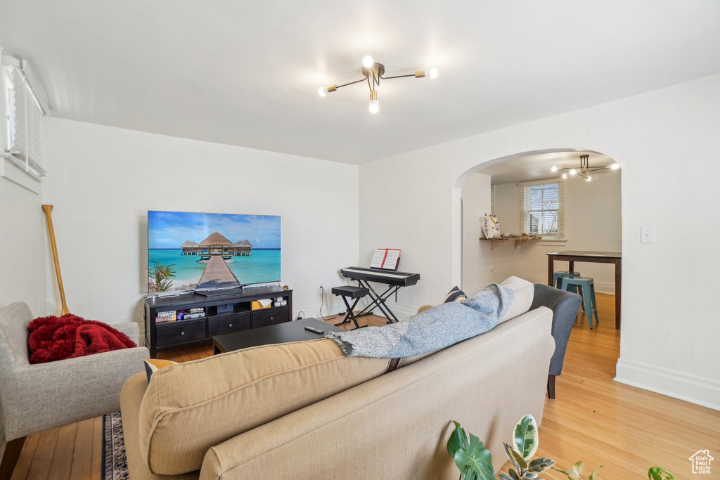 Living room featuring arched walkways, light wood-style flooring, baseboards, and a chandelier