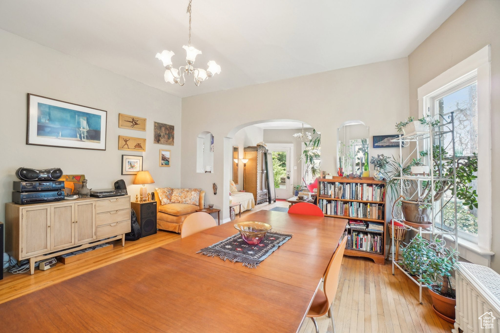 Dining room featuring a chandelier, arched walkways, light wood-style floors, and radiator
