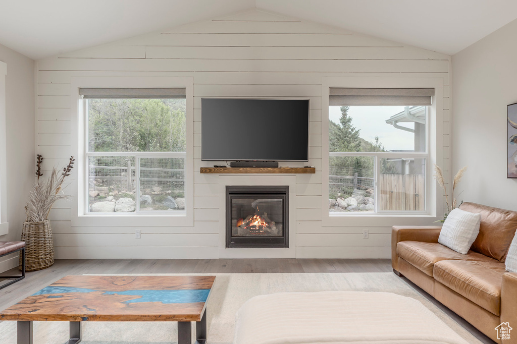 Living room featuring lofted ceiling, wood finished floors, a large fireplace, and wood walls