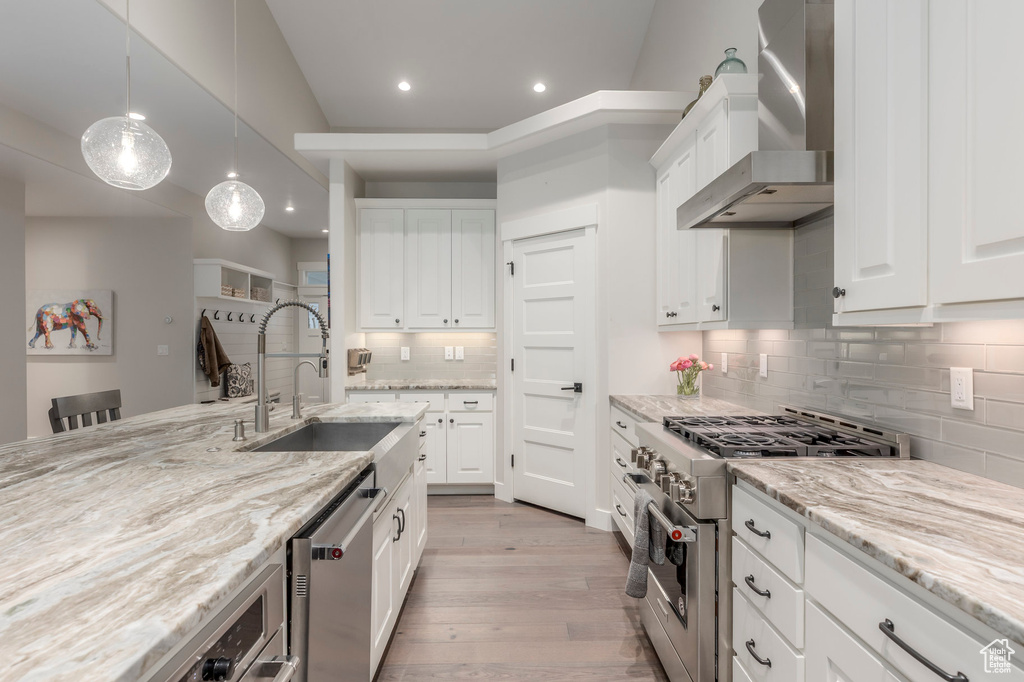 Kitchen featuring appliances with stainless steel finishes, wall chimney exhaust hood, a sink, tasteful backsplash, and light wood finished floors