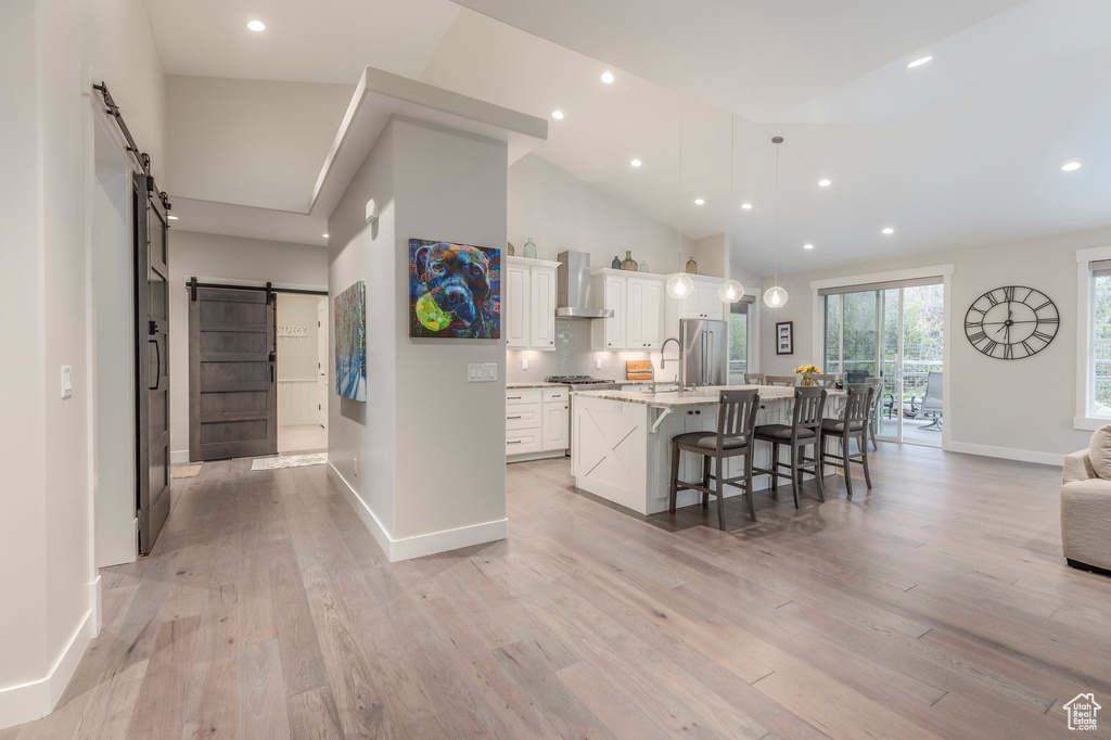 Kitchen with a barn door, wall chimney range hood, baseboards, a large island, and a kitchen breakfast bar