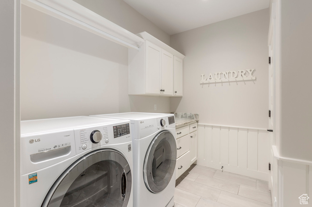 Clothes washing area featuring washer and clothes dryer, cabinet space, and wainscoting