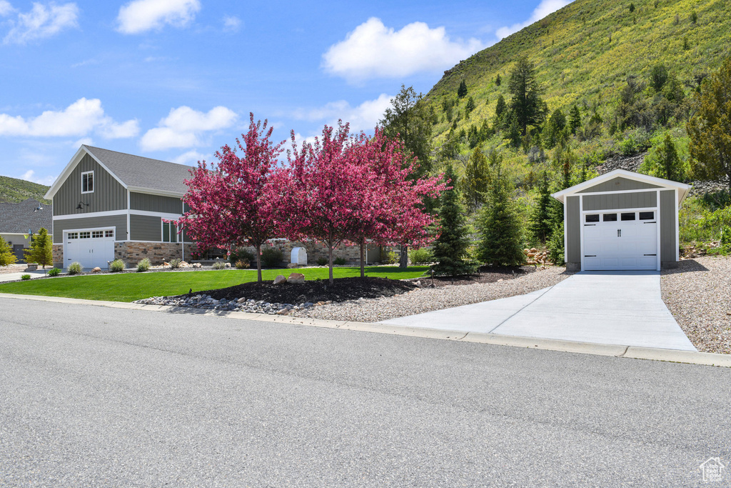 View of front facade with a garage, a front yard, concrete driveway, an outbuilding, and stone siding