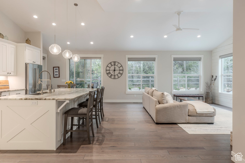 Kitchen featuring a ceiling fan, light stone counters, recessed lighting, wood finished floors, and vaulted ceiling