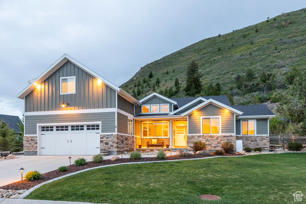 Craftsman-style home featuring stone siding, board and batten siding, a front yard, concrete driveway, and a mountain view