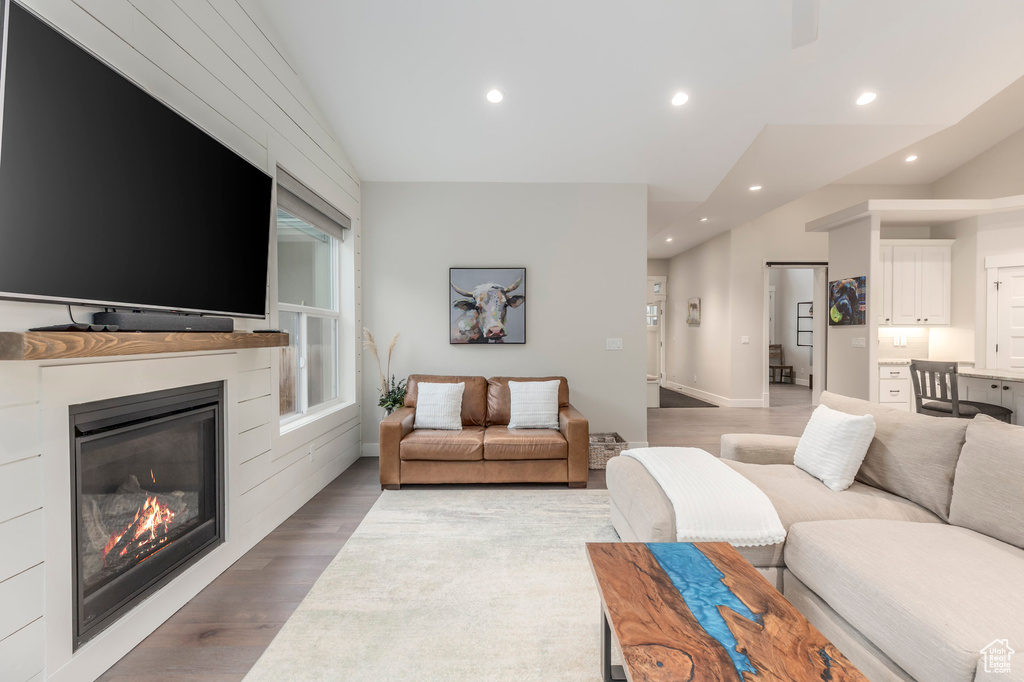 Living room with light wood finished floors, recessed lighting, a glass covered fireplace, vaulted ceiling, and baseboards