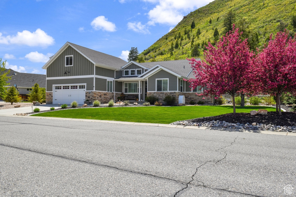 Craftsman-style house with stone siding, board and batten siding, an attached garage, and a front lawn