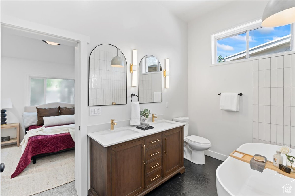 Ensuite bathroom featuring a freestanding tub, double vanity, baseboards, and toilet