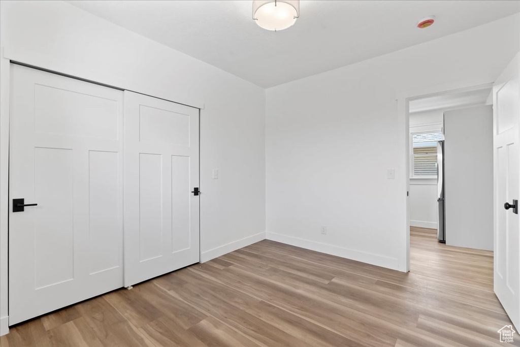 Unfurnished bedroom with light wood-style floors, baseboards, stainless steel refrigerator, and a closet