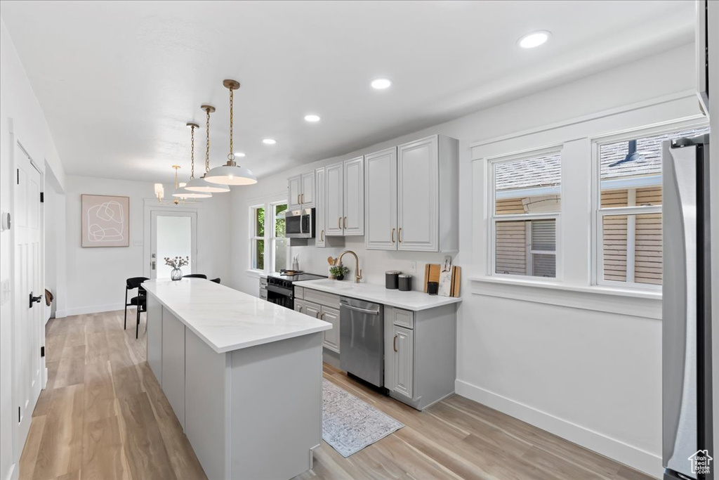 Kitchen featuring stainless steel appliances, a kitchen island, baseboards, light countertops, and light wood-type flooring
