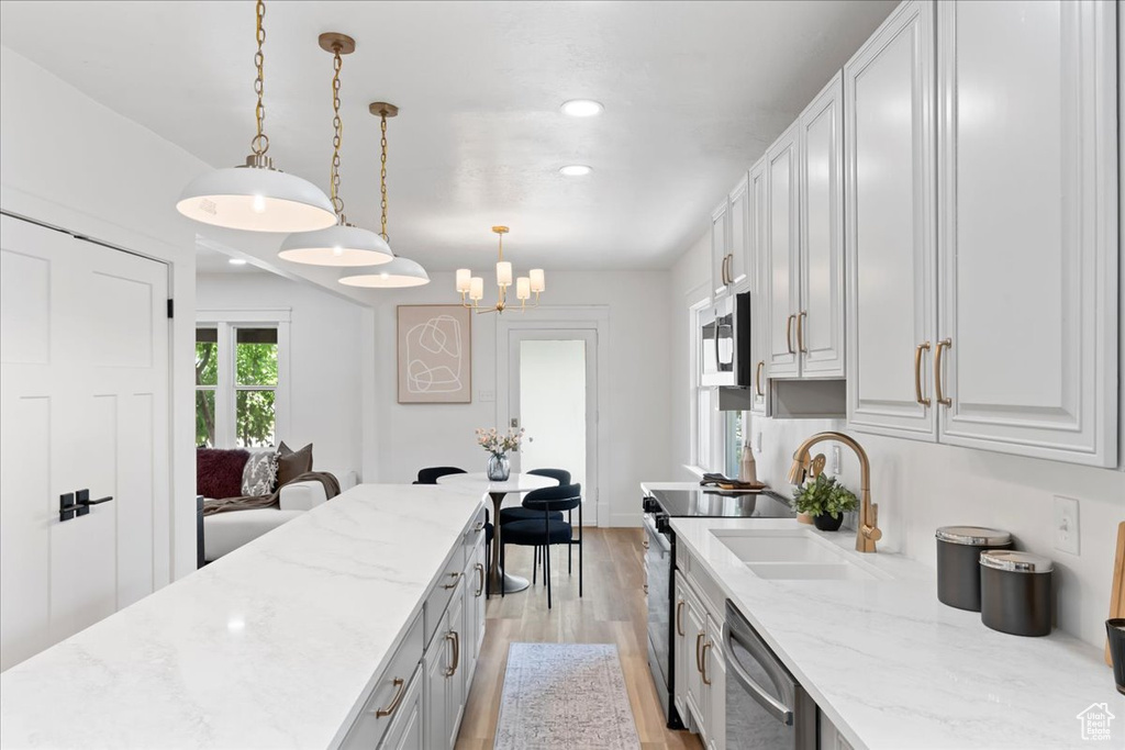 Kitchen with stainless steel appliances, a sink, light wood finished floors, light stone countertops, and recessed lighting