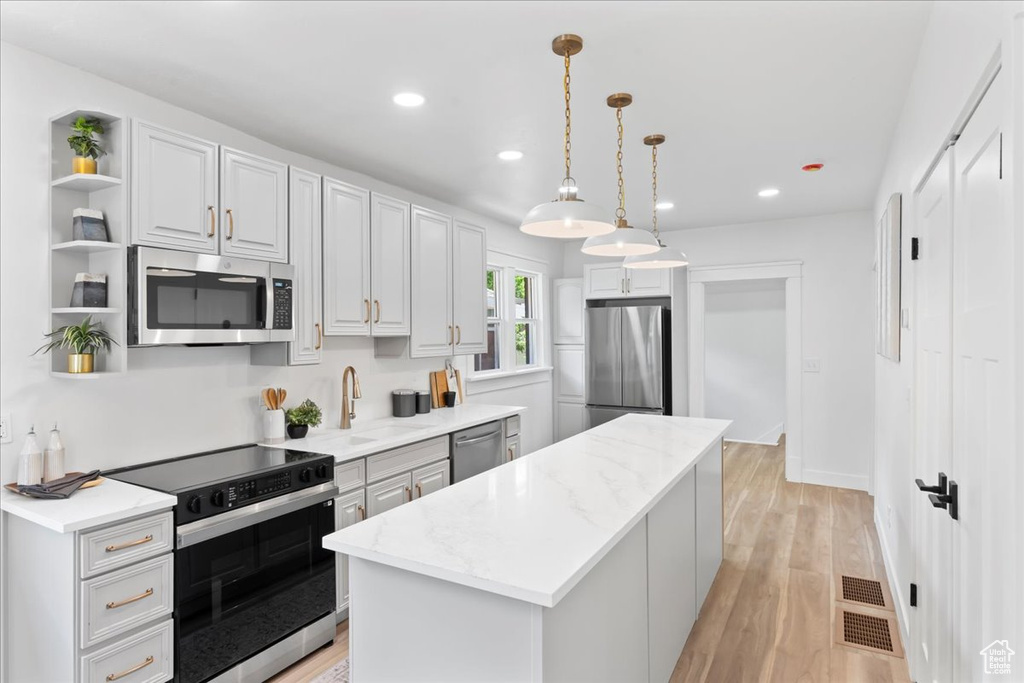 Kitchen with appliances with stainless steel finishes, open shelves, a kitchen island, recessed lighting, and a sink