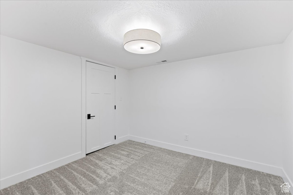 Empty room featuring light carpet, baseboards, and a textured ceiling