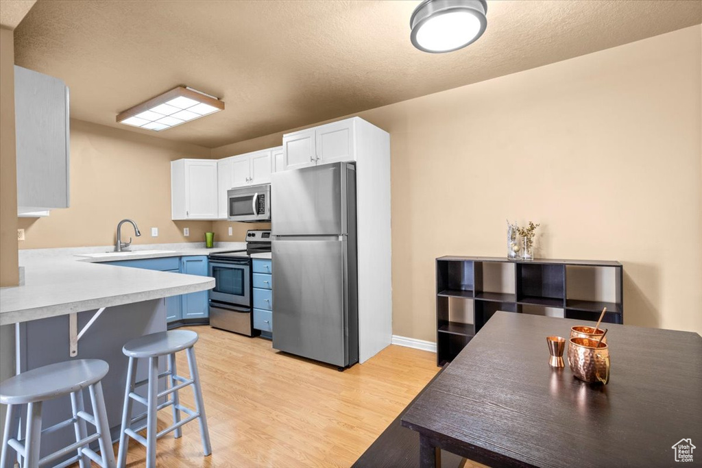 Kitchen with appliances with stainless steel finishes, white cabinets, a kitchen bar, light countertops, and light wood finished floors