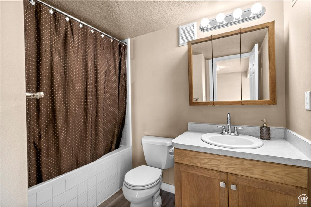 Bathroom with a textured ceiling, toilet, vanity, shower / tub combo, and wood finished floors