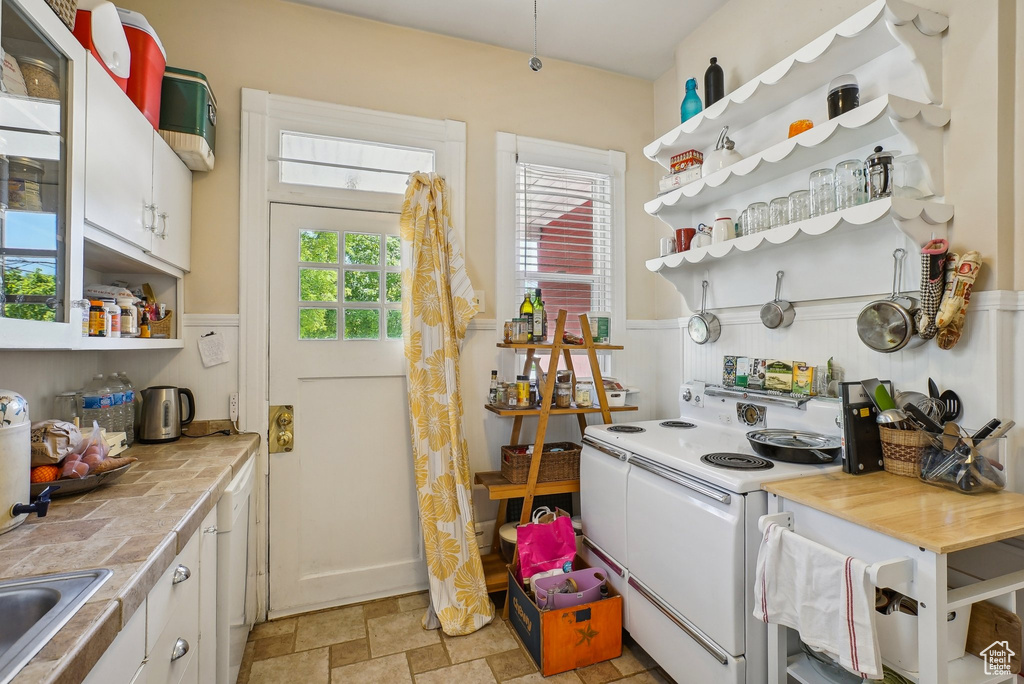 Kitchen featuring white electric range oven, open shelves, a wainscoted wall, white cabinets, and stone finish floors
