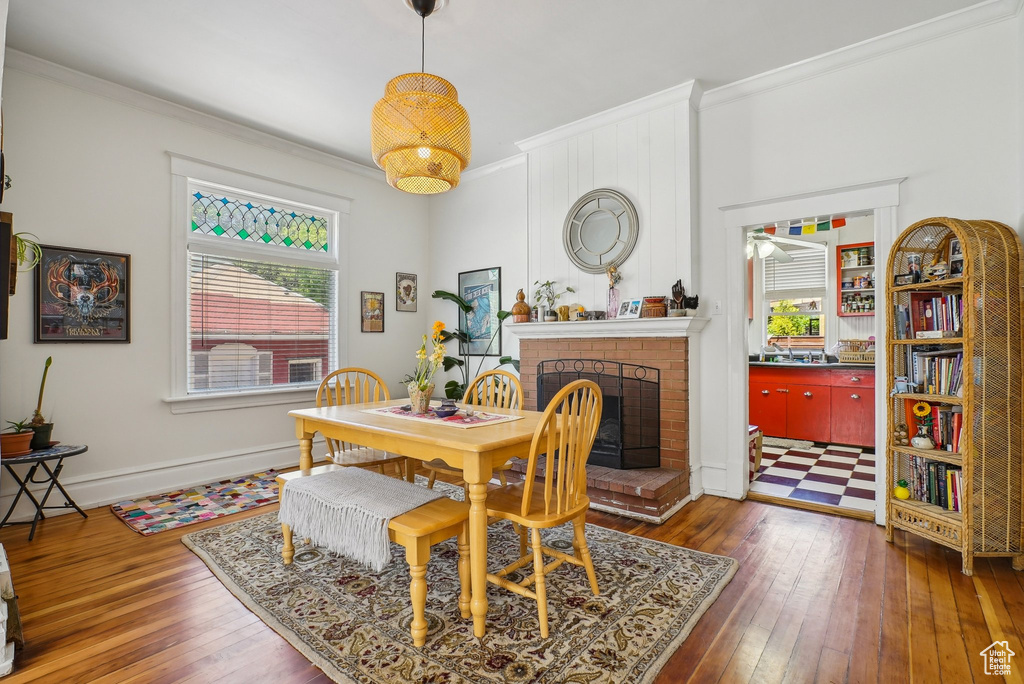 Dining space featuring ornamental molding, a brick fireplace, hardwood / wood-style flooring, a ceiling fan, and baseboards