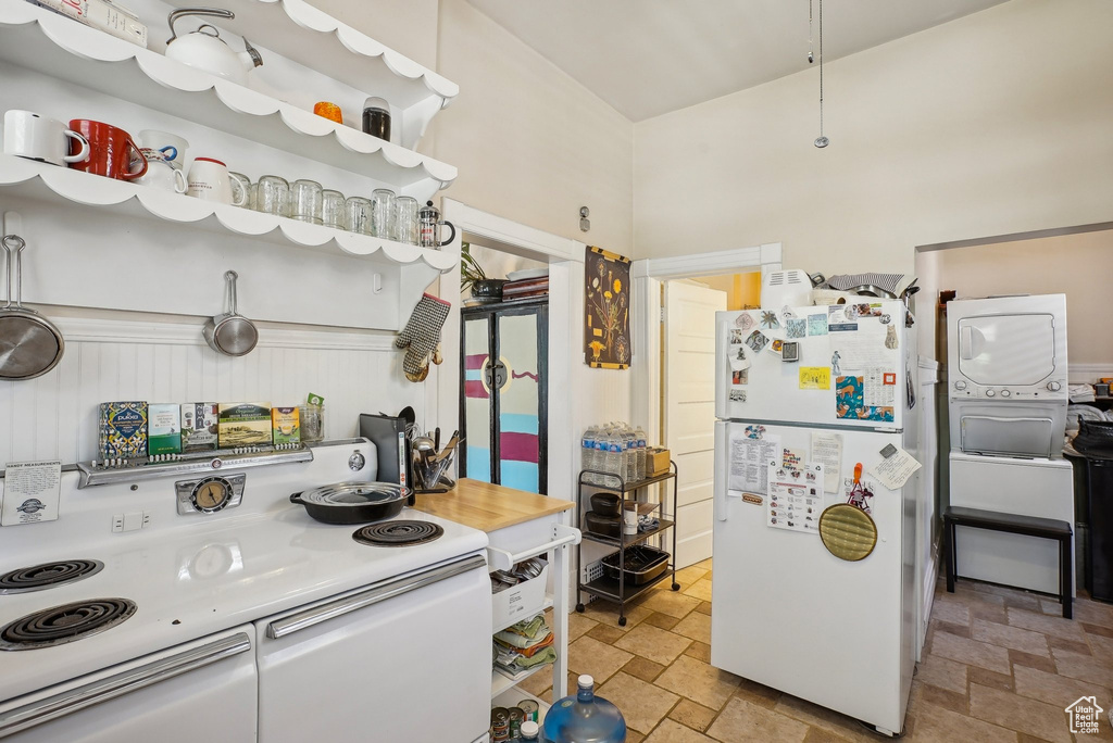 Kitchen featuring white appliances, stacked washing machine and dryer, and stone tile flooring