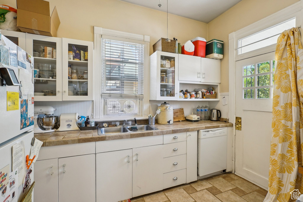 Kitchen with white appliances, white cabinetry, a sink, glass insert cabinets, and stone finish floors