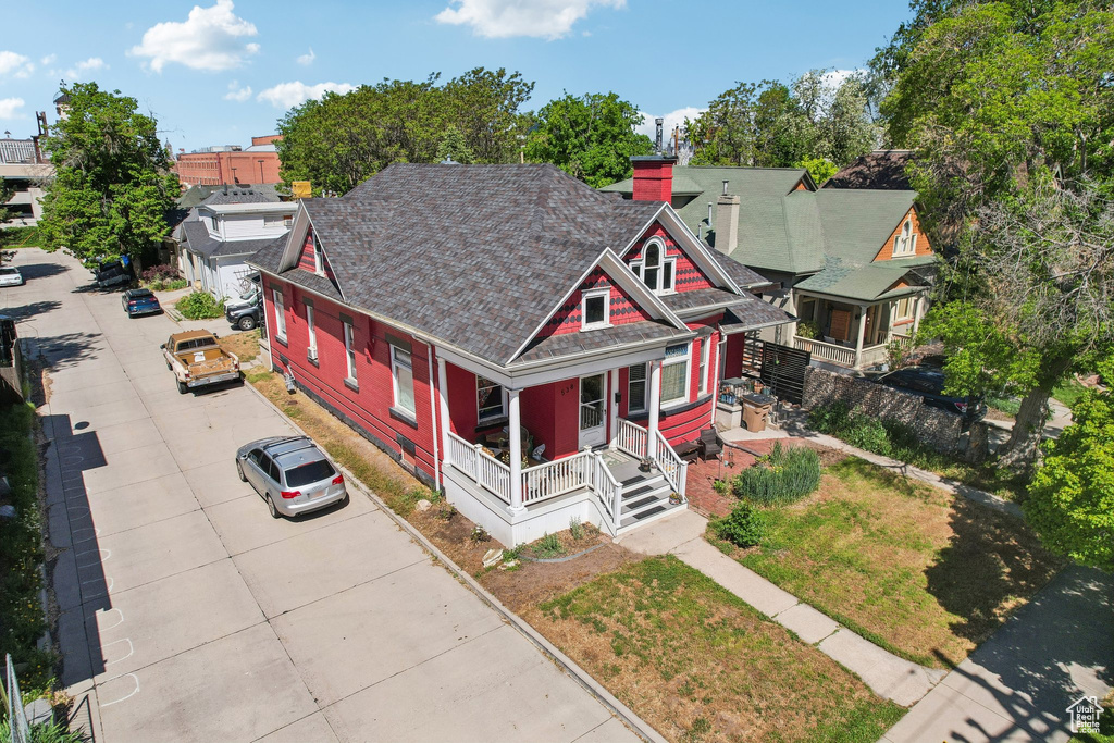 View of front of home with covered porch, a chimney, and roof with shingles