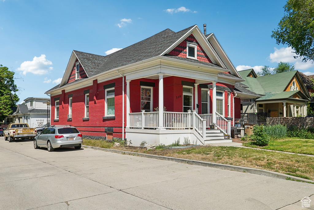 View of front facade featuring a porch, a shingled roof, and brick siding
