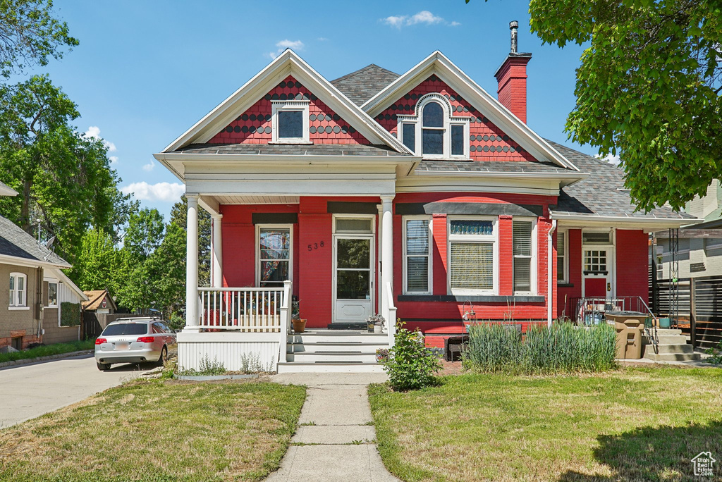 View of front of house featuring covered porch, a front lawn, a chimney, and concrete driveway