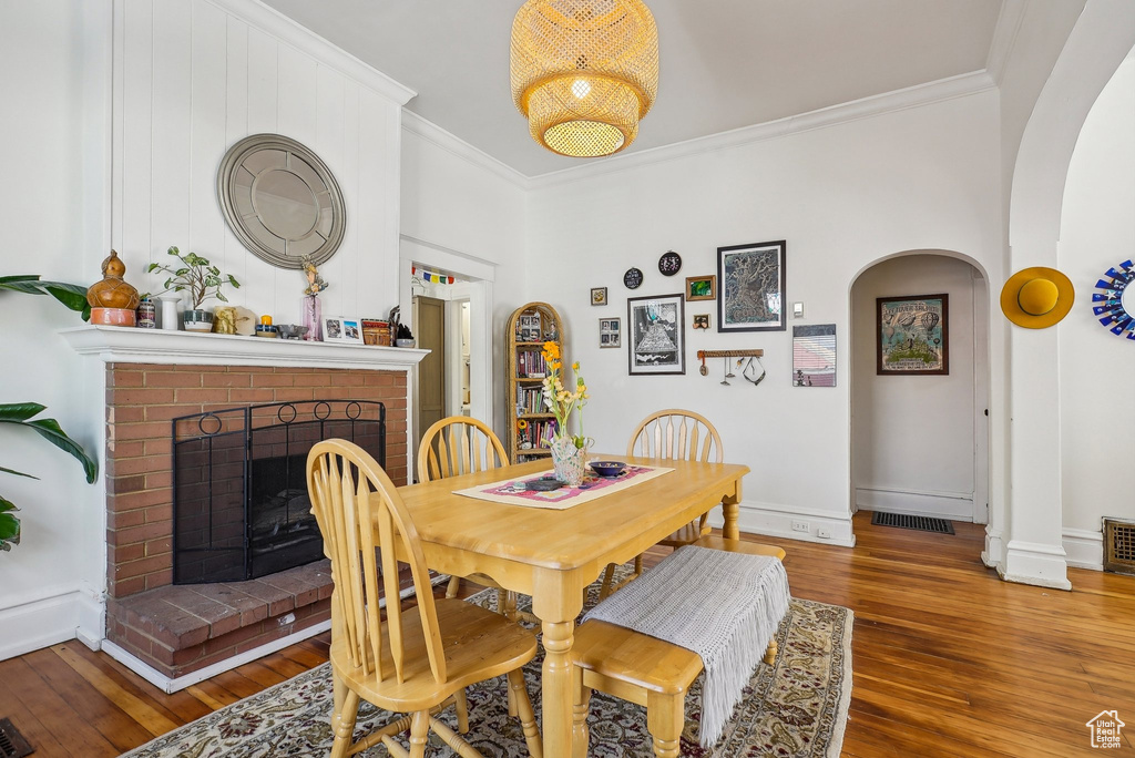Dining area with arched walkways, crown molding, wood finished floors, a brick fireplace, and baseboards