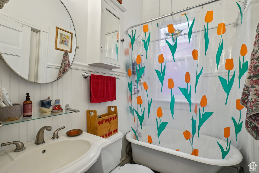 Bathroom featuring a sink, toilet, a decorative wall, and a wainscoted wall