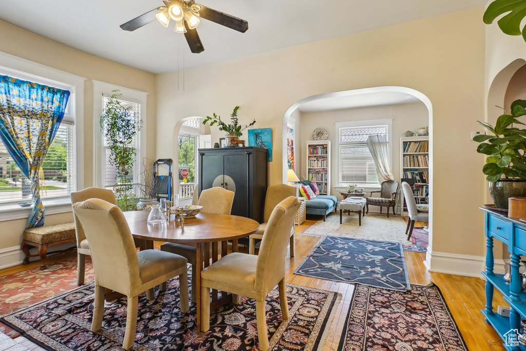 Dining room with ceiling fan, arched walkways, light wood-style floors, and baseboards