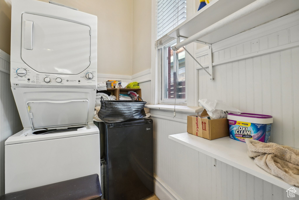Laundry room featuring estacked washer and dryer, a wainscoted wall, and a decorative wall